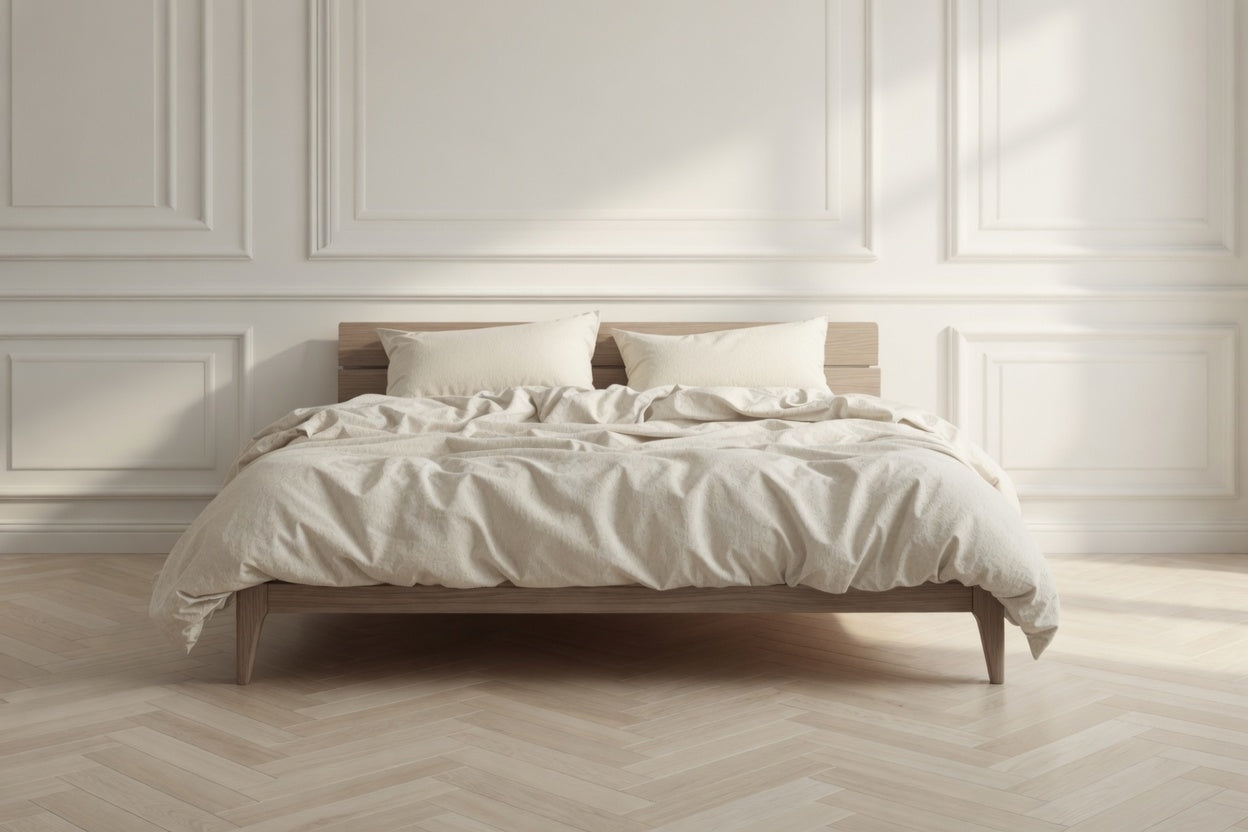 Bedroom with a wooden bed frame and white bedding against a light-colored wall. House of March clotted cream bed linen on the bed.