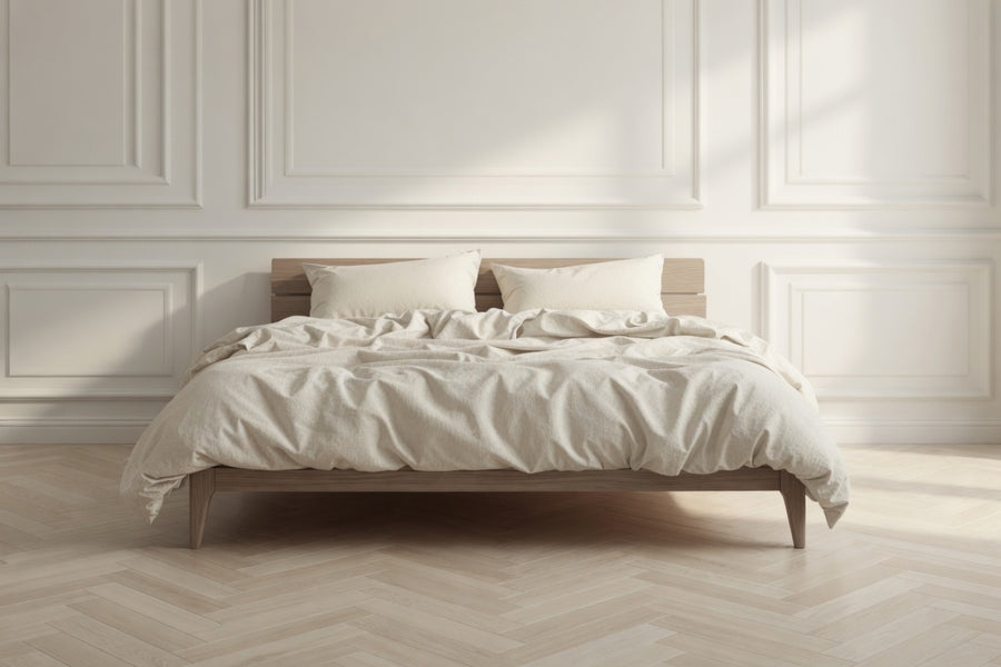 Bedroom with a wooden bed frame and white bedding against a light-colored wall. House of March clotted cream bed linen on the bed.