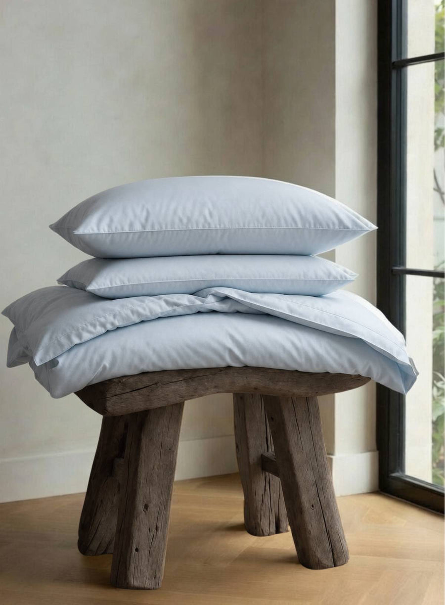 Stack of light blue bedding on a wooden stool against a neutral wall.