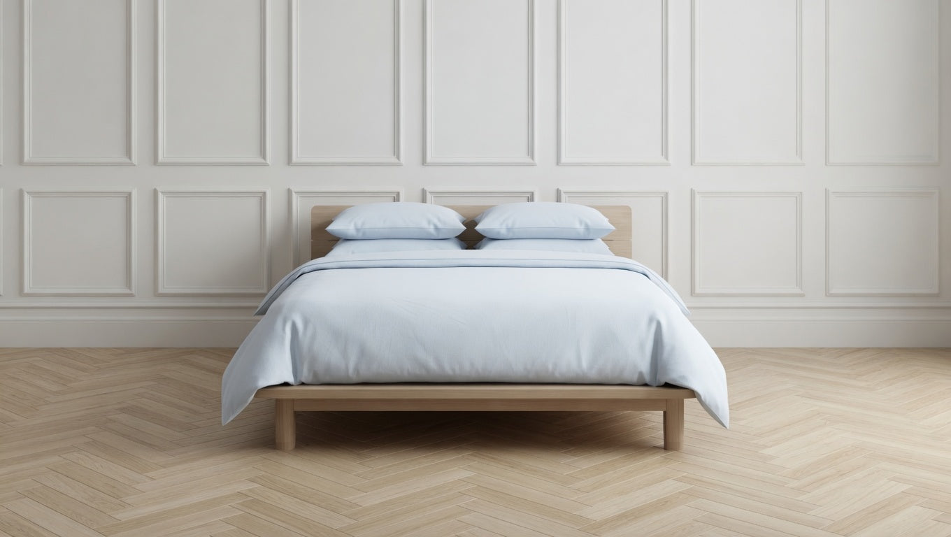 Bed with light blue bedding and pillows against a white paneled wall.