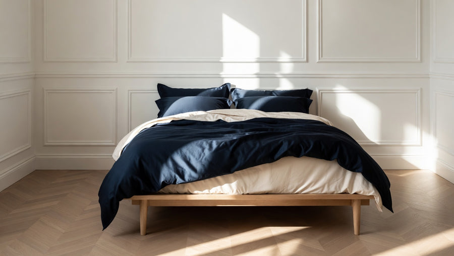 Bed with blue bedding in a room with white paneled walls and wooden flooring.