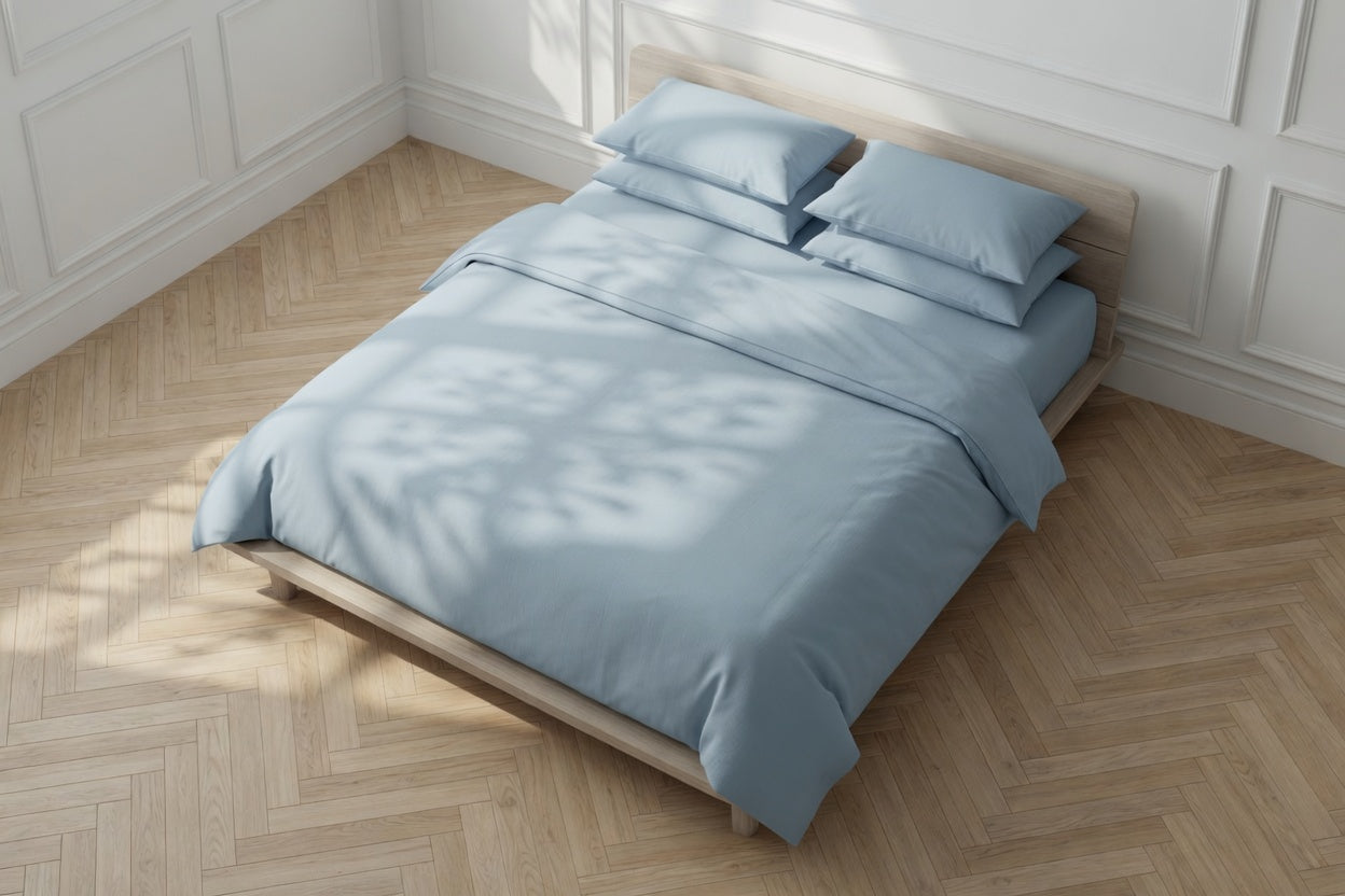 Bed with light blue organic hoUSE OF MARCH bedding in a room with wooden flooring and white walls.