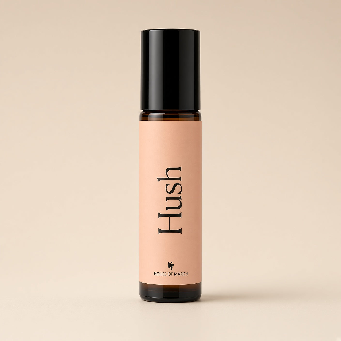 A small amber glass roller bottle with a black cap and a peach-pink label reading 'Hush' and 'HOUSE OF MARSH', centered on a warm beige background.