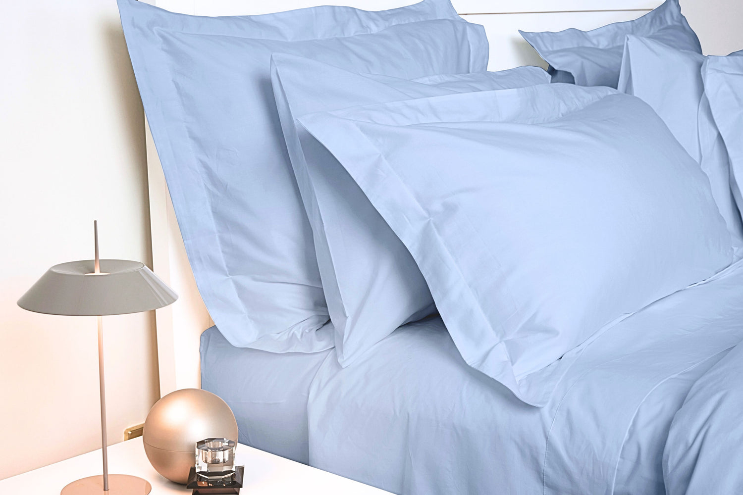 A set of blue pillowcases with Oxford border displayed on a bed, with a lamp and ornament on the bedside table by House of March