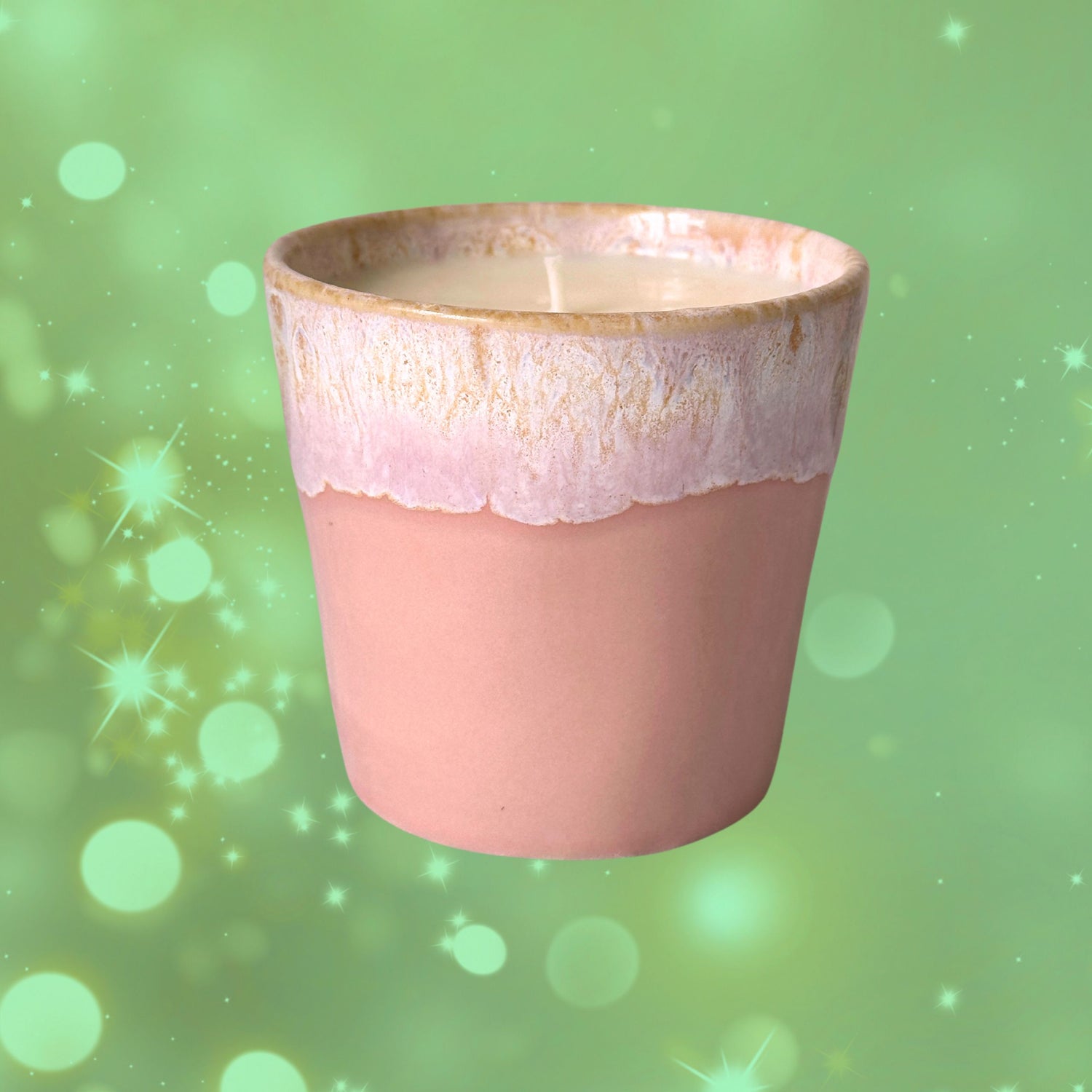 A blush pink coffee cup candle with a white rim, floating against a green sparkling background.