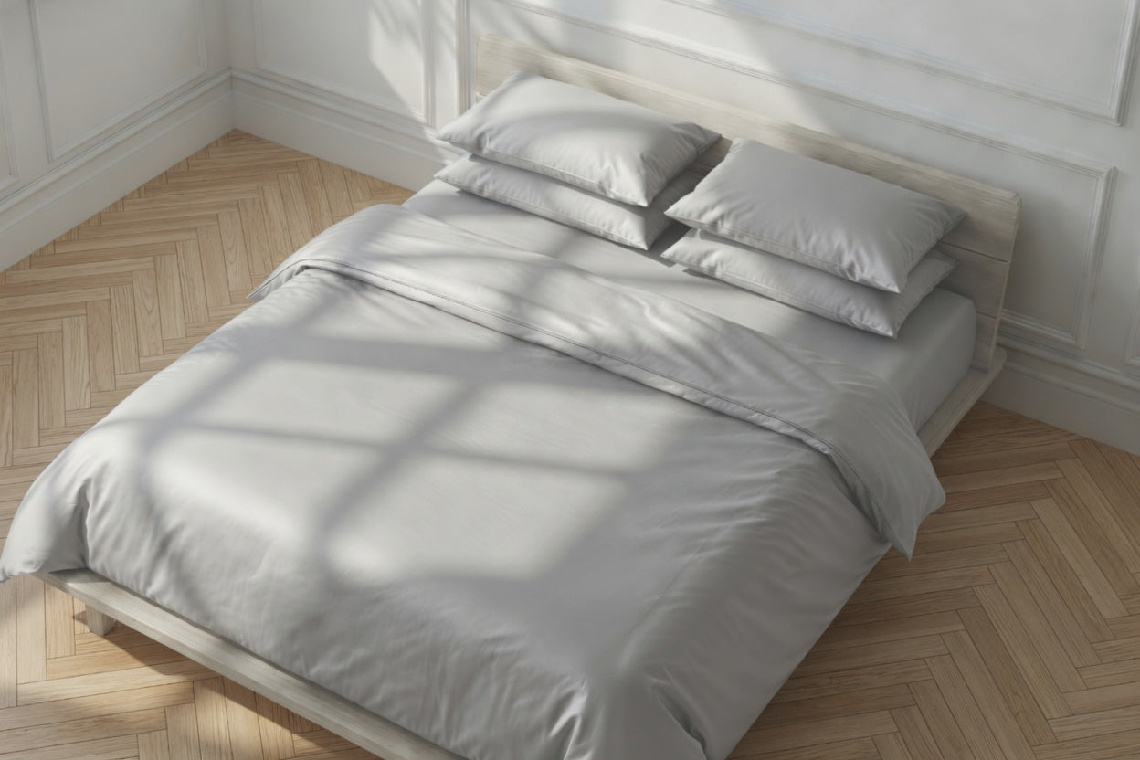 Gray bedding set on a bed in a room with wooden flooring and white walls.