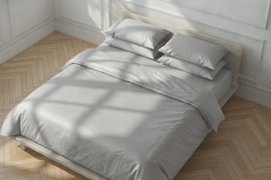 Gray bedding set on a bed in a room with wooden flooring and white walls.