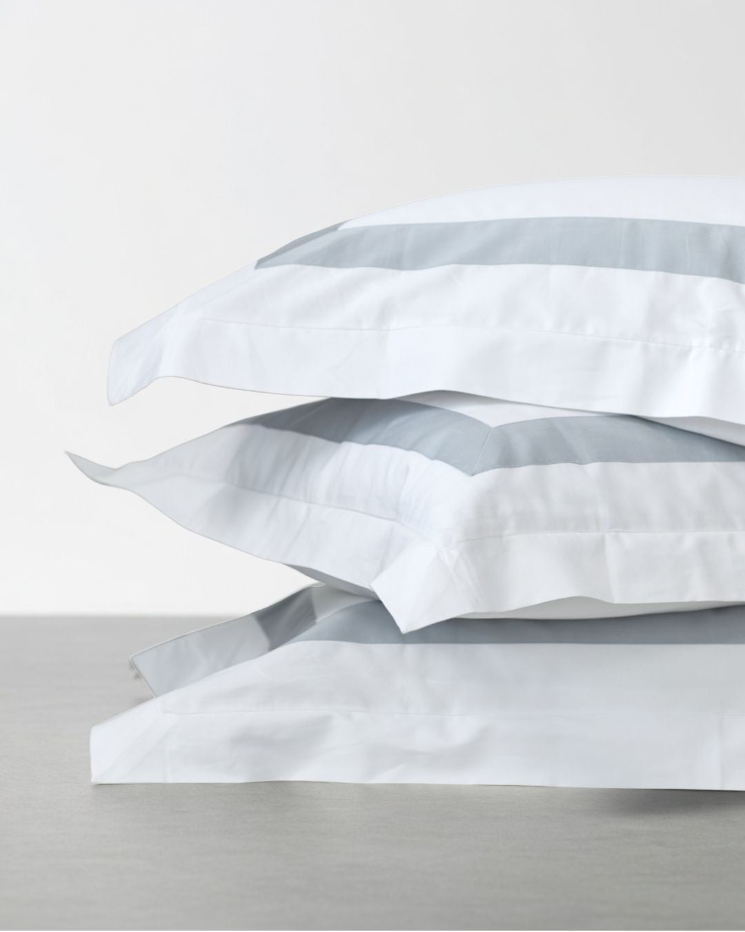 Stack of white and sky blue organic banded pillowscaseswith blue stripes on a light gray background