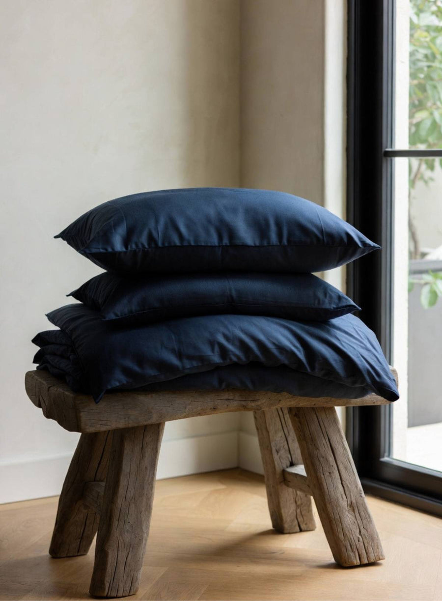 Stack of organic navy blue pillows on a wooden stool by a window