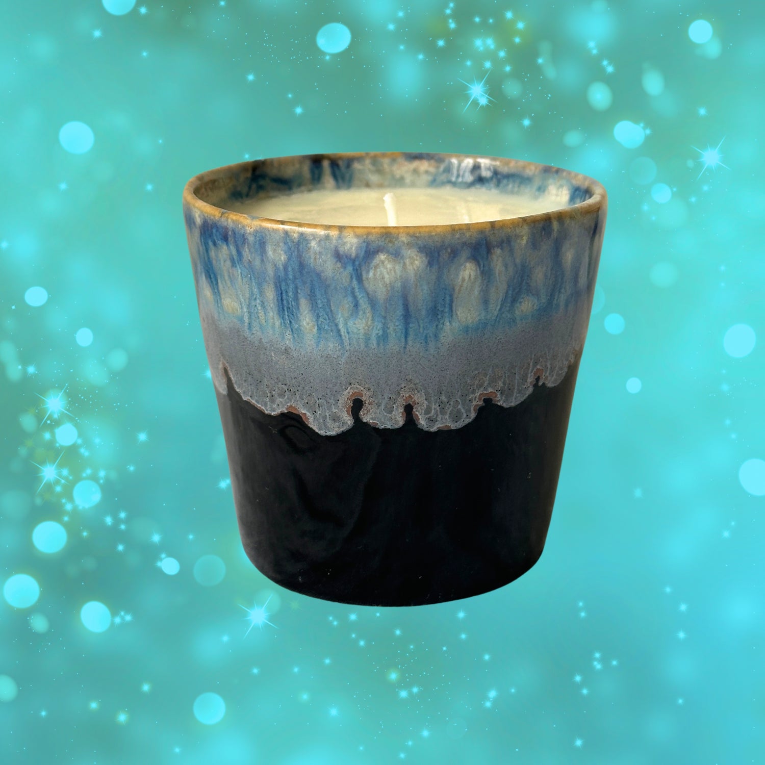 A ceramic coffee cup candle with a blue and black glaze, filled with white wax, on a blue background with bokeh lights.