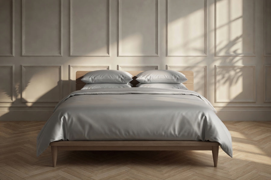 Bed with gray bedding and pillows in a room with wooden flooring and paneled walls.