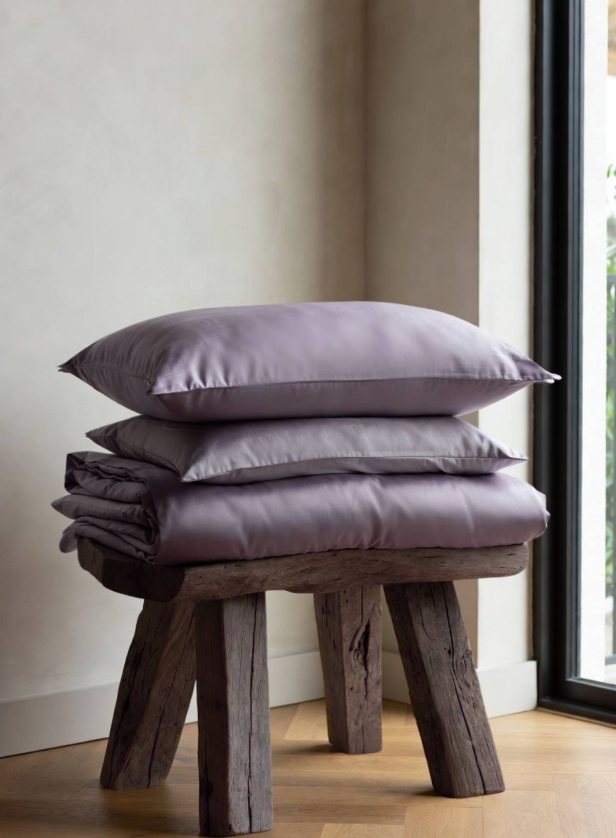 Stack of purple pillows on a wooden stool against a neutral wall.