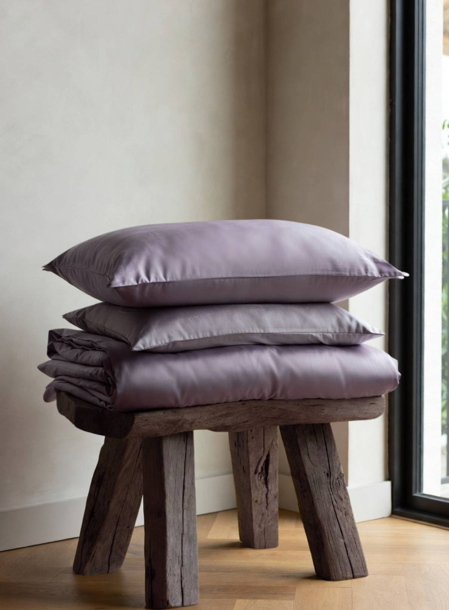 Stack of purple pillows on a wooden stool against a neutral wall.